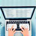 Personne écrivant dans un carnet avec un ordinateur portable.